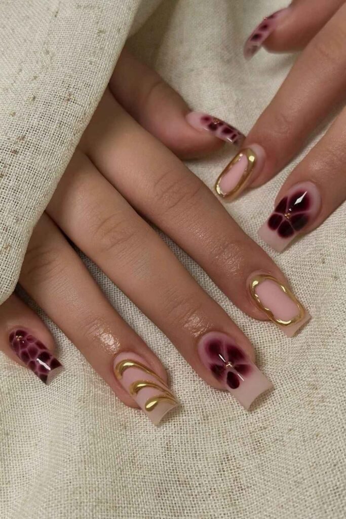 Neutral nails with burgundy blooming florals and gold chrome details