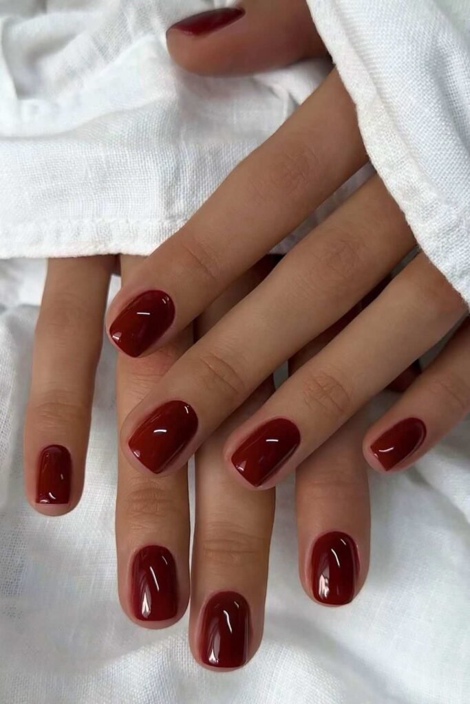 Short glossy burgundy manicure on white fabric