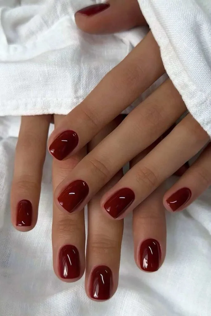 Short glossy burgundy manicure on white fabric